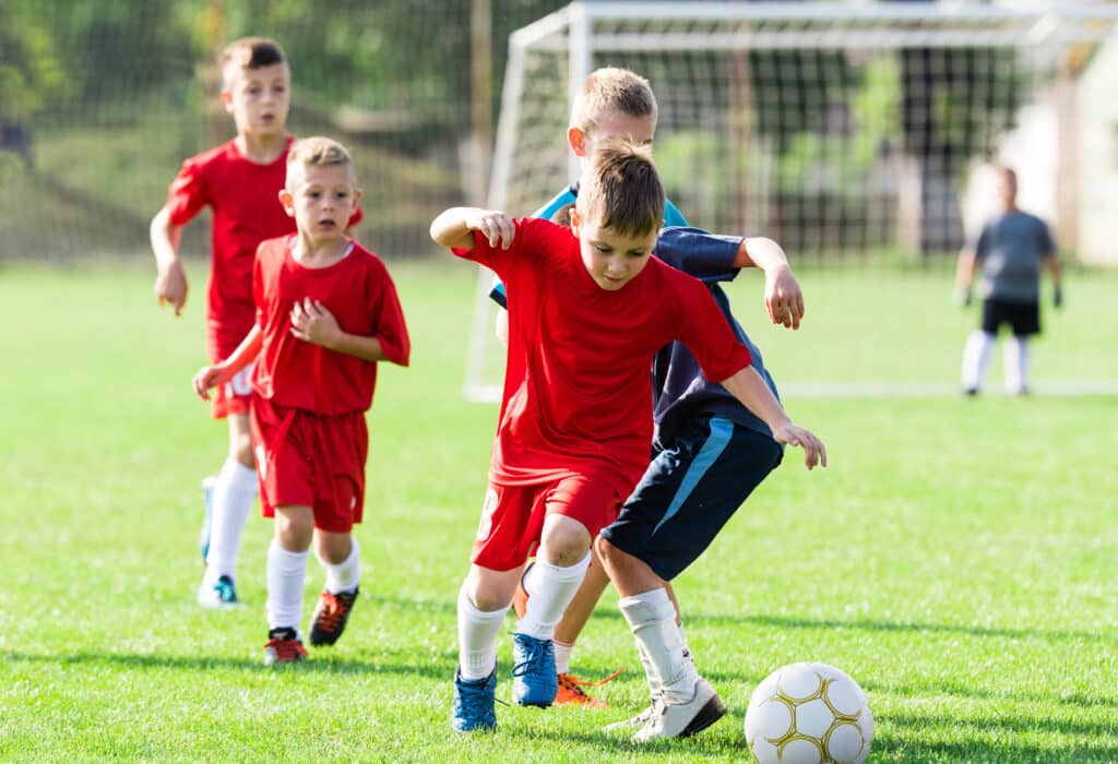 Pojkar i röda lagtröjor som spelar fotboll på en fotbollsplan. Ett mål syns i bakgrunden